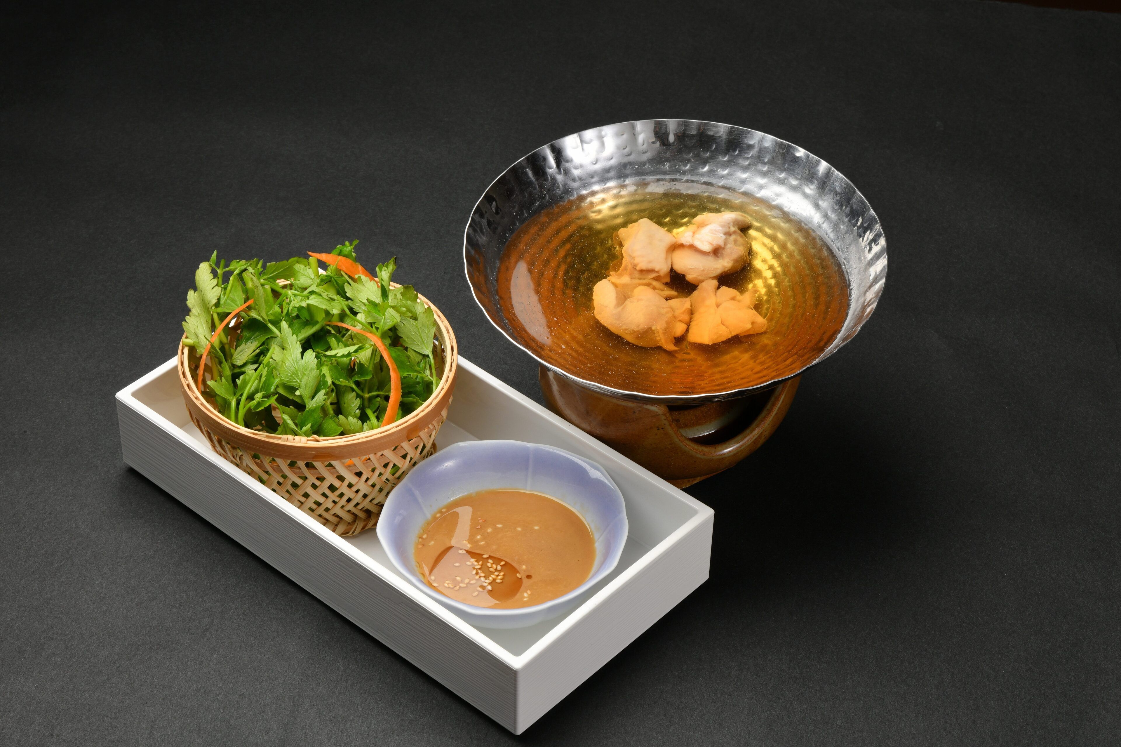 A tray with a bowl of soup, a bowl of sauce, and a basket of greens.