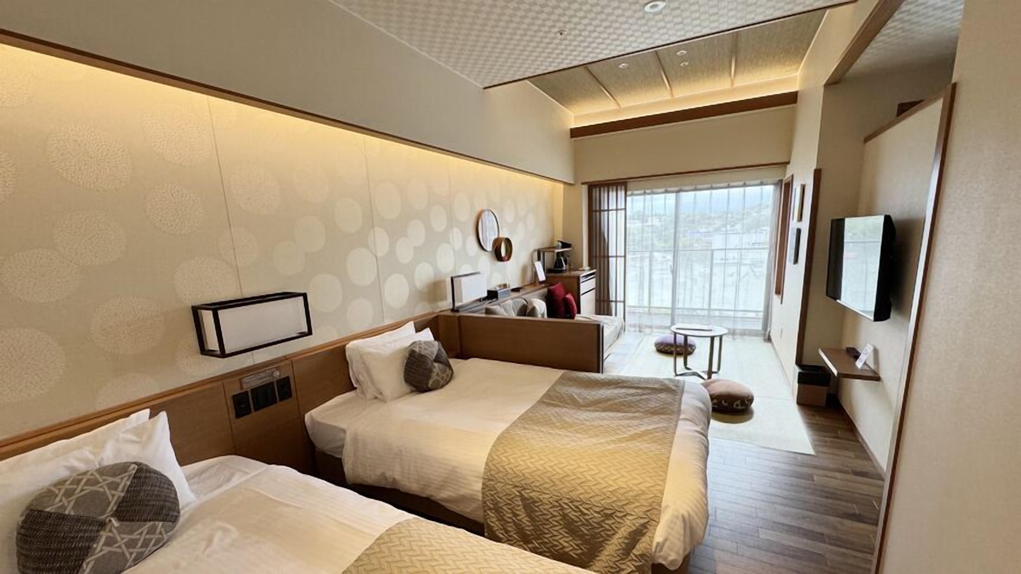 A hotel room with two beds, a desk, a television, and a large window.