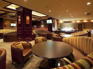 Un vestíbulo de hotel con zonas de estar, un bar y una pantalla de televisión.