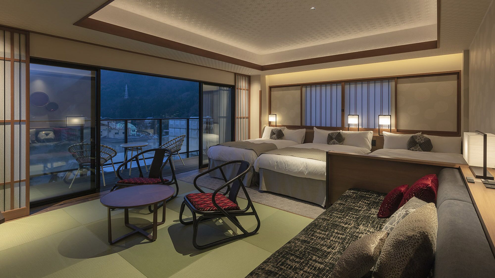 A hotel room with a balcony, a bed, a sofa, and a dining table.