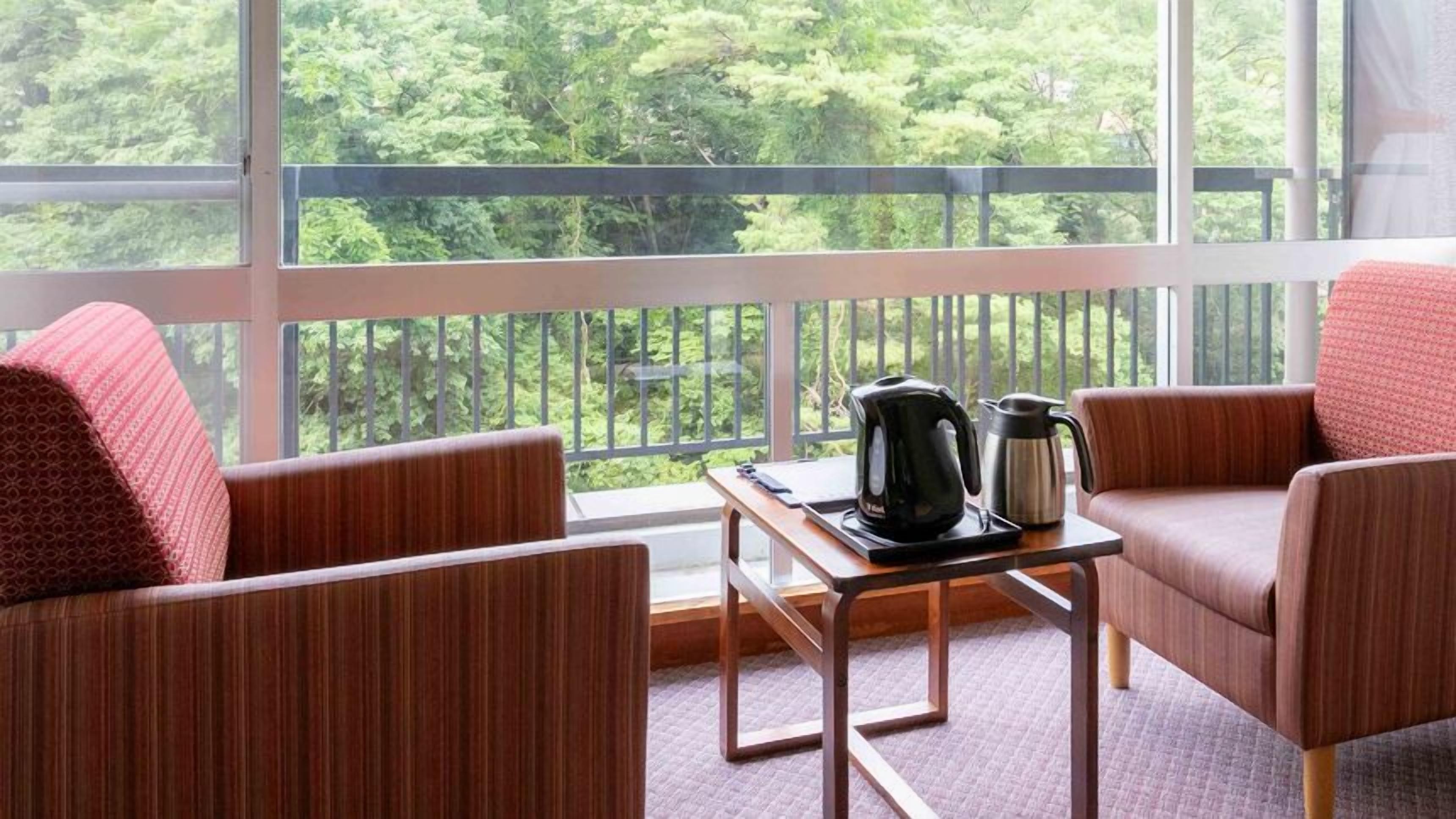 A balcony with two chairs, a table, a kettle, and a coffee pot.