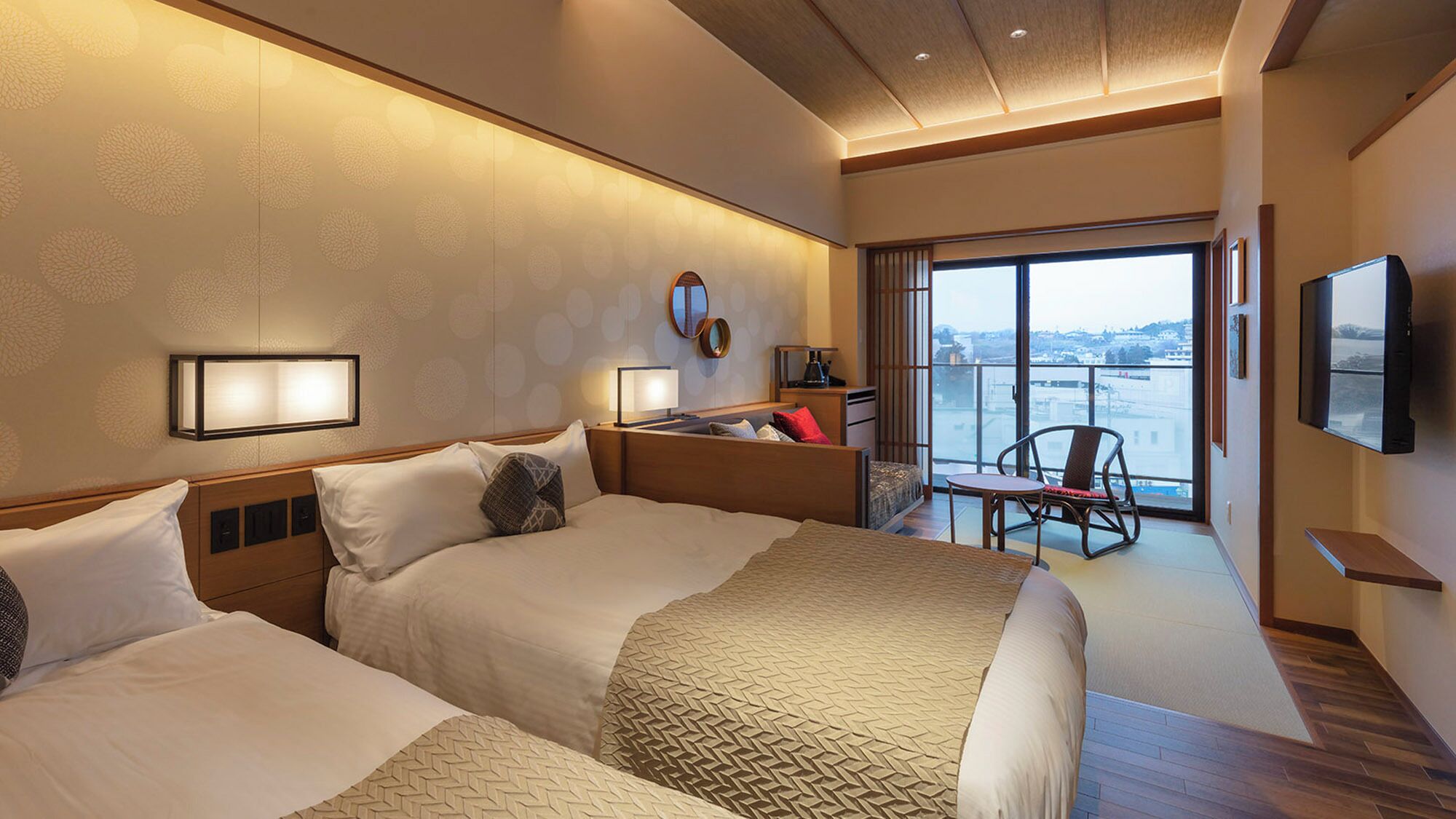 A hotel room with two beds, a desk, a chair, a TV, and a balcony with a view.
