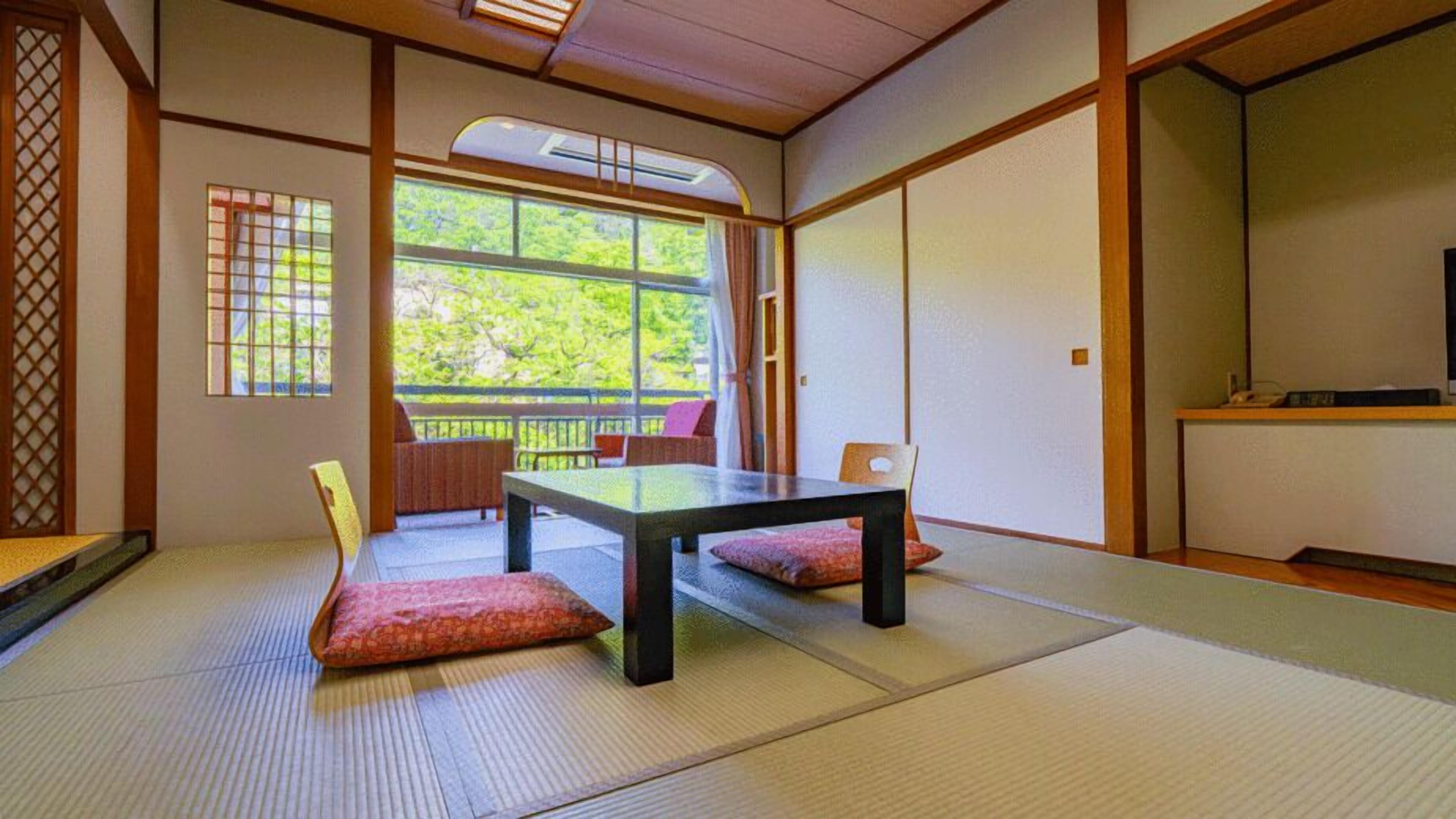 A tatami mat room with a low table, chairs, and a sliding door leading to a balcony.