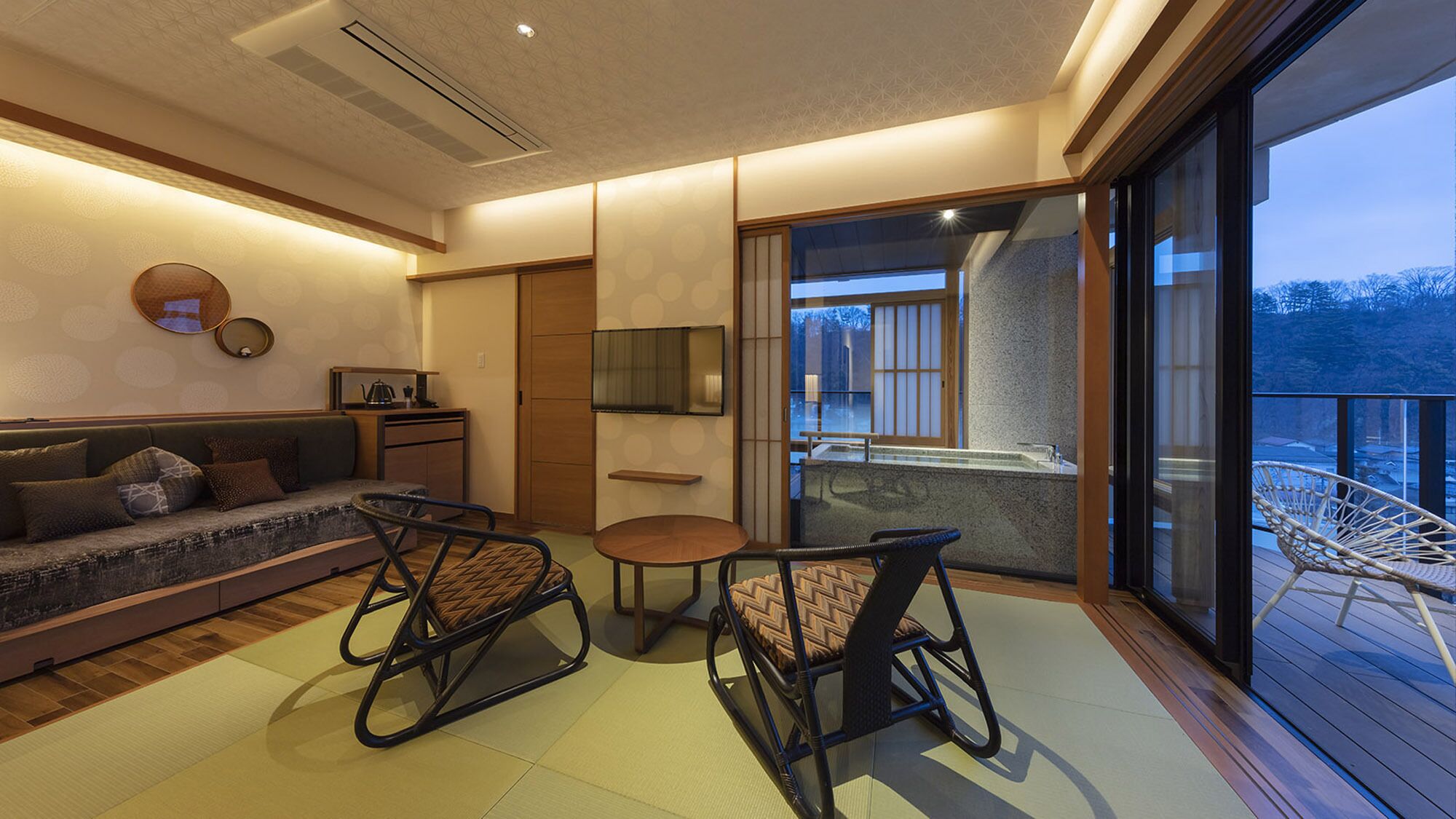 A modern interior with a sofa, two chairs, a small table, a TV, and a balcony with a view.