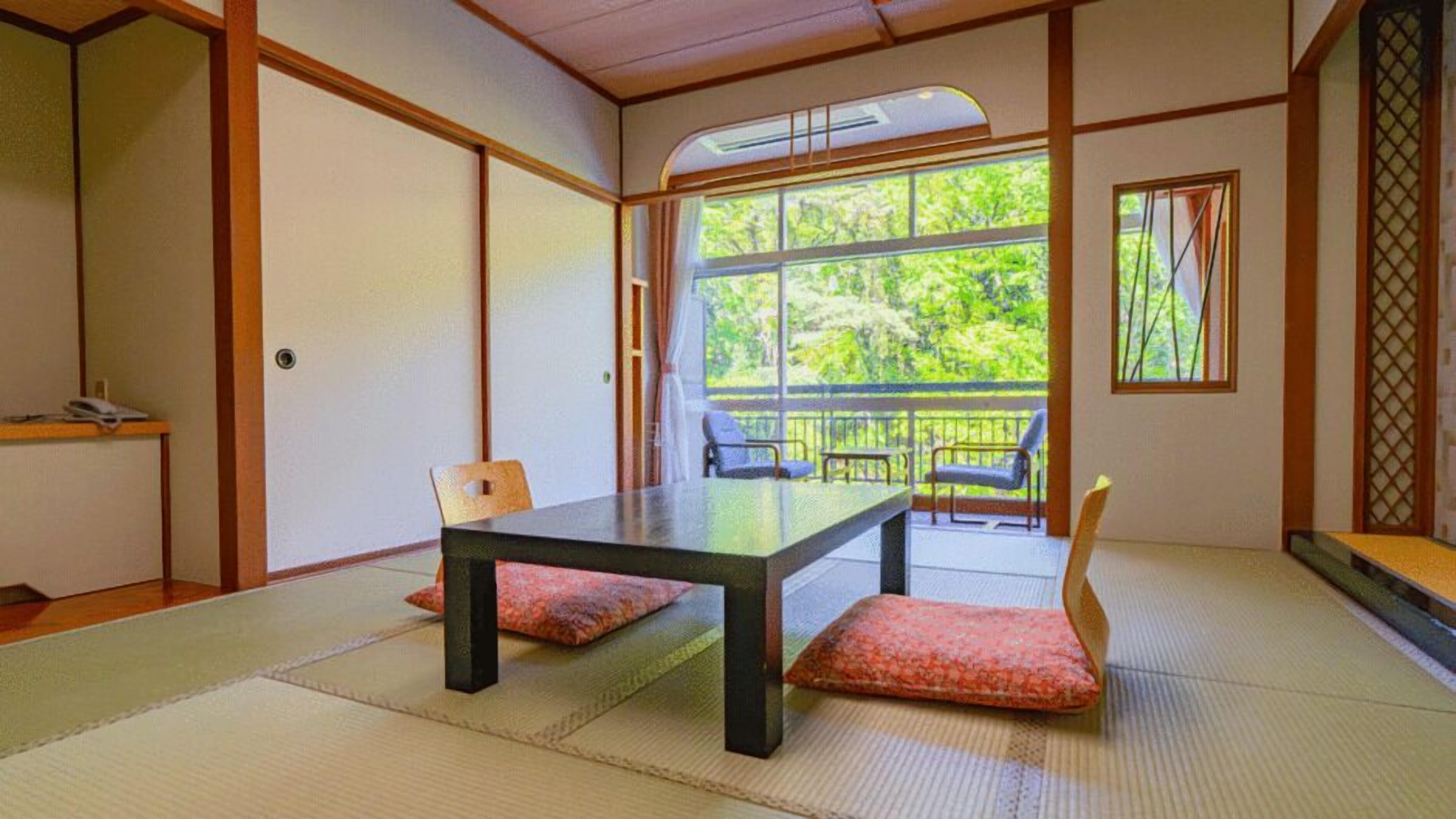 A traditional Japanese room with tatami flooring, a low table, and a view of greenery through large windows.