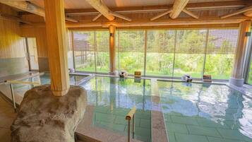An indoor swimming pool with clear glass walls, wooden beams, and a stone feature.