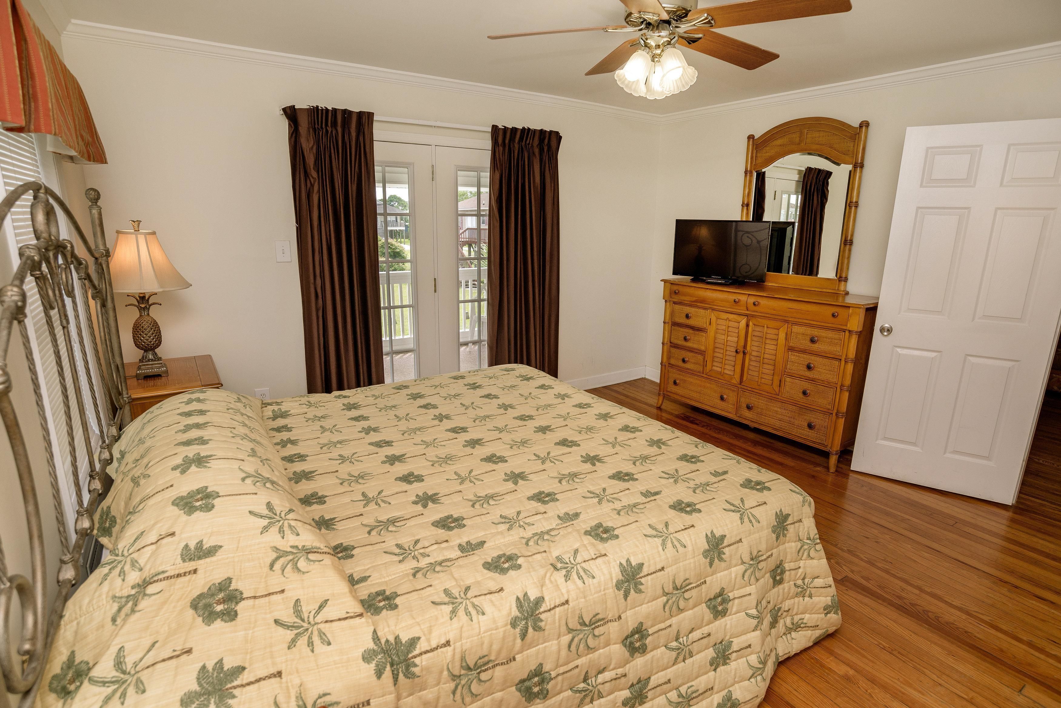 A bedroom with a bed, a wooden dresser, a television, and a ceiling fan.