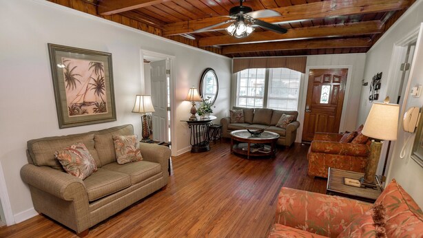 A cozy living room with a wooden ceiling, a sofa, a coffee table, and a patterned armchair. - At Last Apartment 5 (Murrells Inlet)