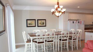 A dining area with a wooden table and white chairs, a chandelier, and two framed pictures on the wall. - Bermuda Breeze C Holiday Home Holiday home 8 (North Myrtle Beach)