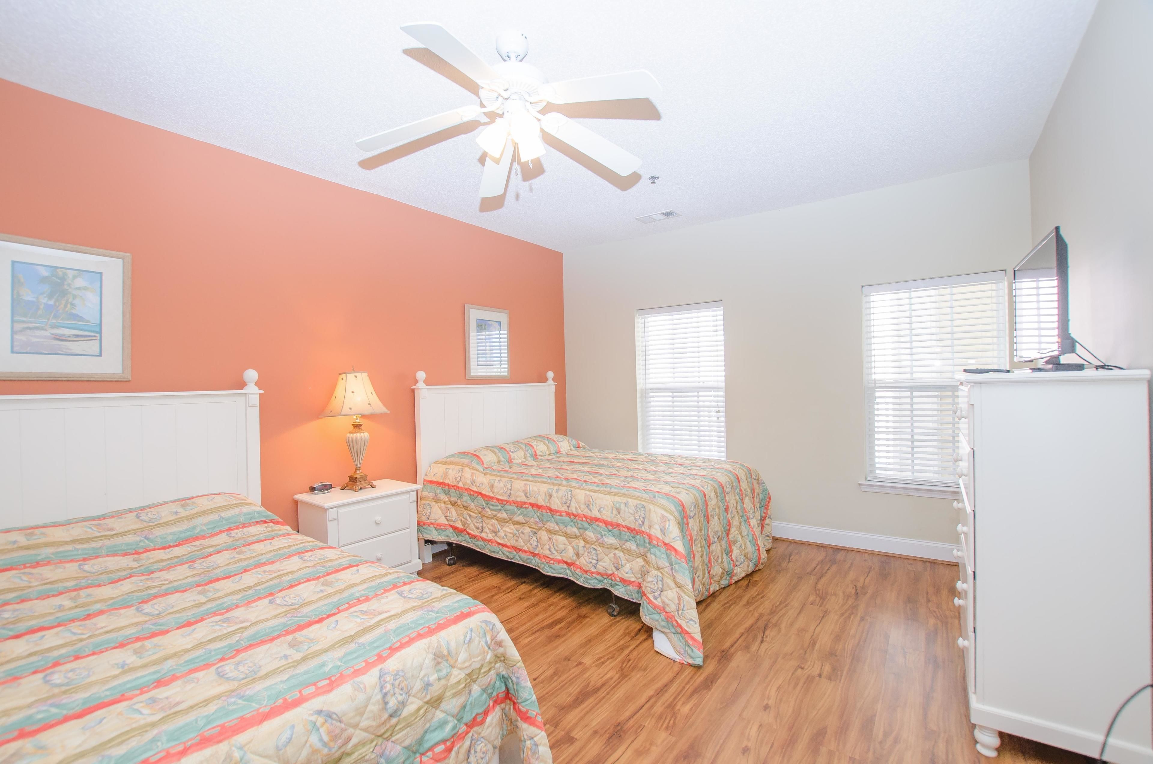 A bedroom with two beds, a ceiling fan, a dresser, and a window with blinds.