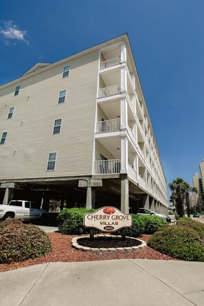 Un hôtel à plusieurs étages doté d’un balcon au deuxième étage, d’une enseigne indiquant « Cherry Grove Villas 200 », et d’un espace de stationnement à l’avant.