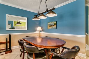 Un coin repas comprenant une table ronde en bois, six chaises en cuir, un luminaire suspendu, un miroir fixé au mur et un tableau encadré.