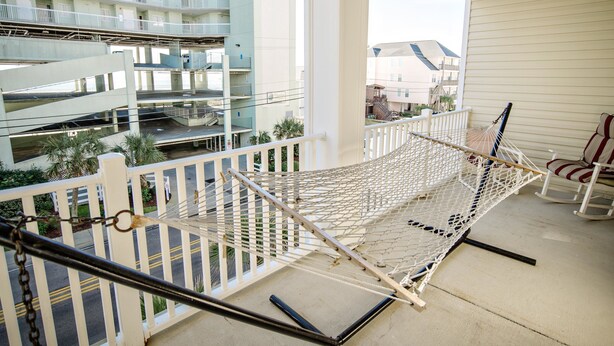 A balcony with a hammock, white railing, and a view of a multi-story building.