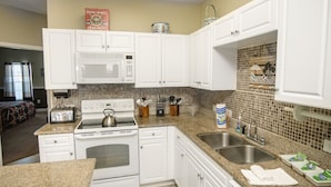 A kitchen with white cabinets, a microwave, a stove, and a sink. There is a book titled 'Ships Wheel Crabmeat' on the wall.