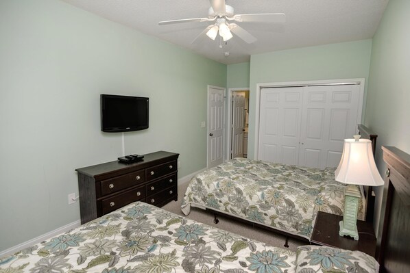 A bedroom with two beds, a ceiling fan, a TV, a dresser, and a door.