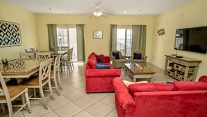 A spacious living room with a red sofa, a dining table with chairs, a television, and a ceiling fan. - Cherry Grove 406 Villa Villa 6 (North Myrtle Beach)