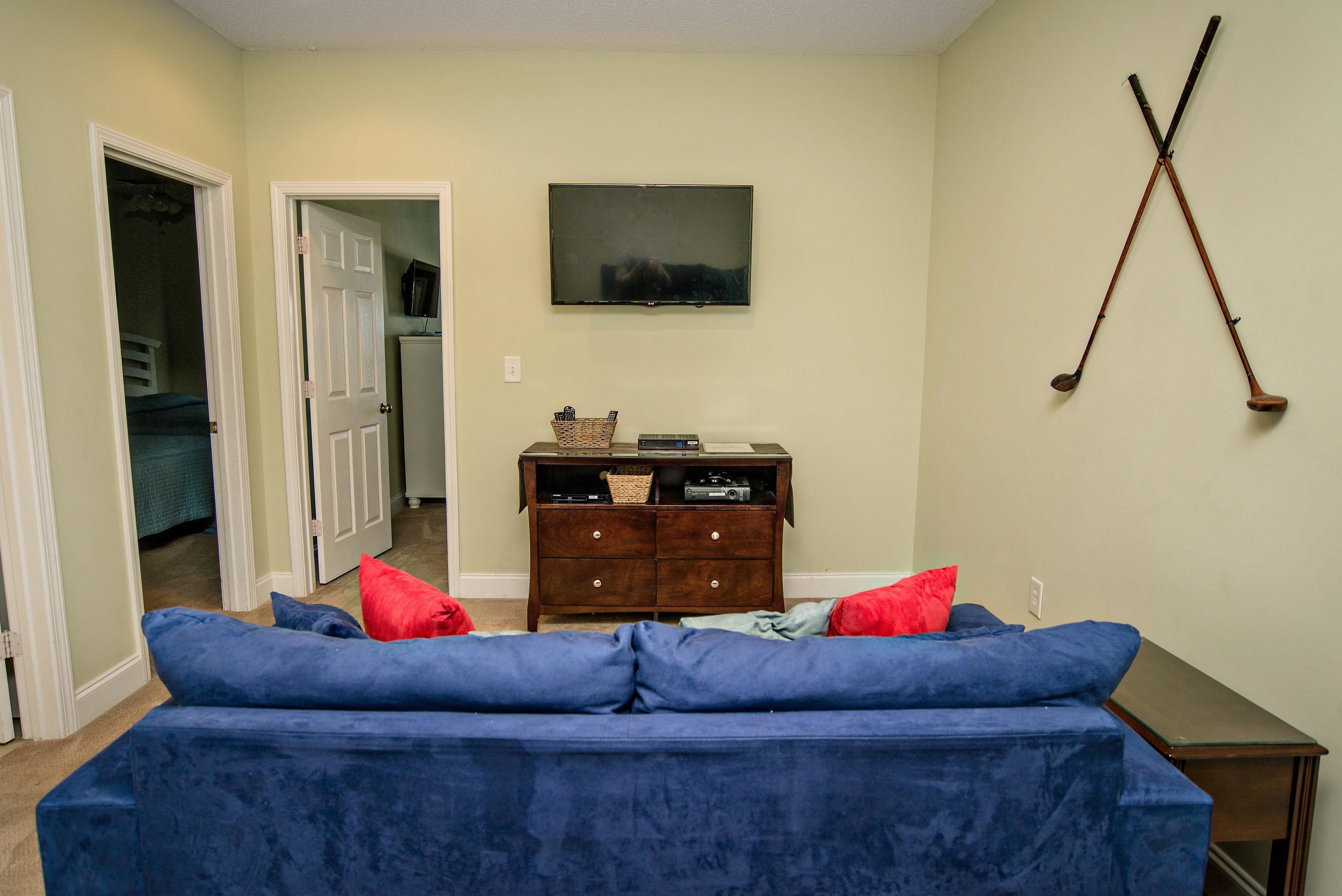 A living room with a blue sofa, a wooden cabinet, and a television on the wall.