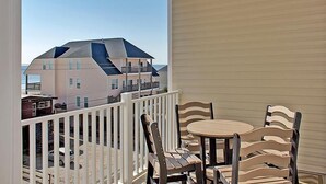 A balcony with a white railing, a round table, and four striped chairs. - Cherry Grove 406 Villa Villa 6 (North Myrtle Beach)