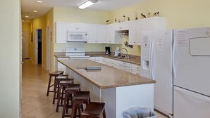 A kitchen with white cabinets, a central island with stools, and a refrigerator. - Cherry Grove 406 Villa Villa 6 (North Myrtle Beach)