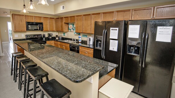 A modern kitchen with granite countertops, stainless steel appliances, wooden cabinets, and bar stools. - Coconut Grove 204 Villa Villa 5 (North Myrtle Beach)