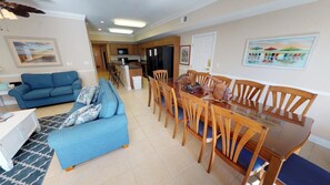 A living room with a blue sofa and a dining area with wooden chairs and a glass table. - Coconut Grove 205 Villa Villa 6 (North Myrtle Beach)