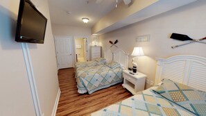 A bedroom with two beds, a TV mounted on the wall, and a sailboat decoration. - Coconut Grove 205 Villa Villa 6 (North Myrtle Beach)