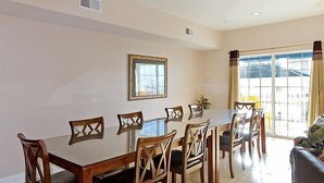A dining area with a large table and chairs, a window with curtains, and a view of the outside. - Coconut Grove 402 Villa Villa 6 (North Myrtle Beach)