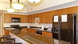 A modern kitchen with wooden cabinets, a granite countertop, a black refrigerator, and a built-in microwave. - Coconut Grove 402 Villa Villa 6 (North Myrtle Beach)