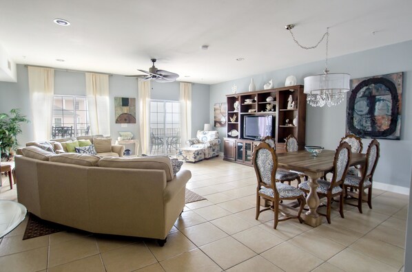 A spacious living room with a beige sofa, dining table with chairs, and a television.