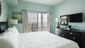 A bedroom with a bed, a dresser, a TV, a window with curtains, and a painting on the wall. - Coconut Grove 403 Villa Villa 5 (North Myrtle Beach)