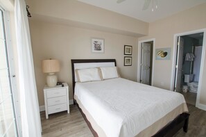 A bedroom with a bed, bedside table, lamp, and a door leading to a bathroom.