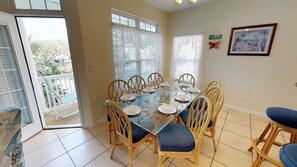 Uma área de refeições com mesa de vidro, cadeiras de vime e vista para o exterior.