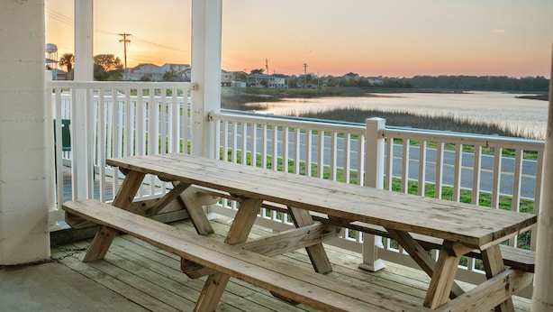 A wooden picnic table on a porch with a view of a body of water and houses in the background. - Grand Cayman C Holiday Home Holiday home 8 (North Myrtle Beach)