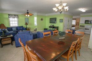 A spacious living room with a large wooden dining table, blue sofas, and a ceiling fan.