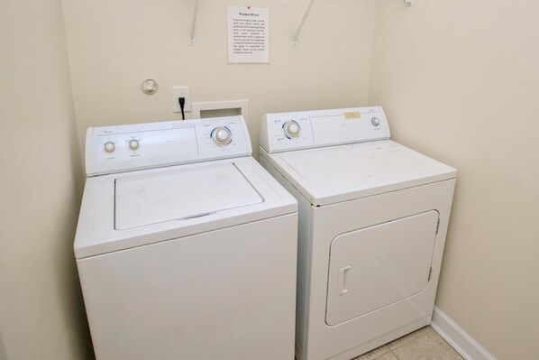 Two white front-loading washers in a laundry room with a sign above them.