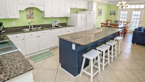 A kitchen with white cabinets, a granite countertop, a central island with stools, and a refrigerator. - Grand Cayman C Holiday Home Holiday home 8 (North Myrtle Beach)