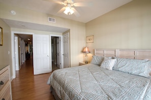 A bedroom with a large bed, a nightstand, a lamp, and a ceiling fan.
