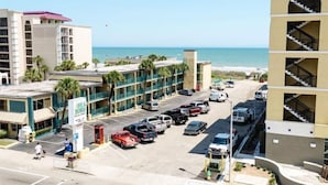 Ein Hotel mit Parkplatz, Blick auf den Strand und einem mehrstöckigen Gebäude mit Balkonen.