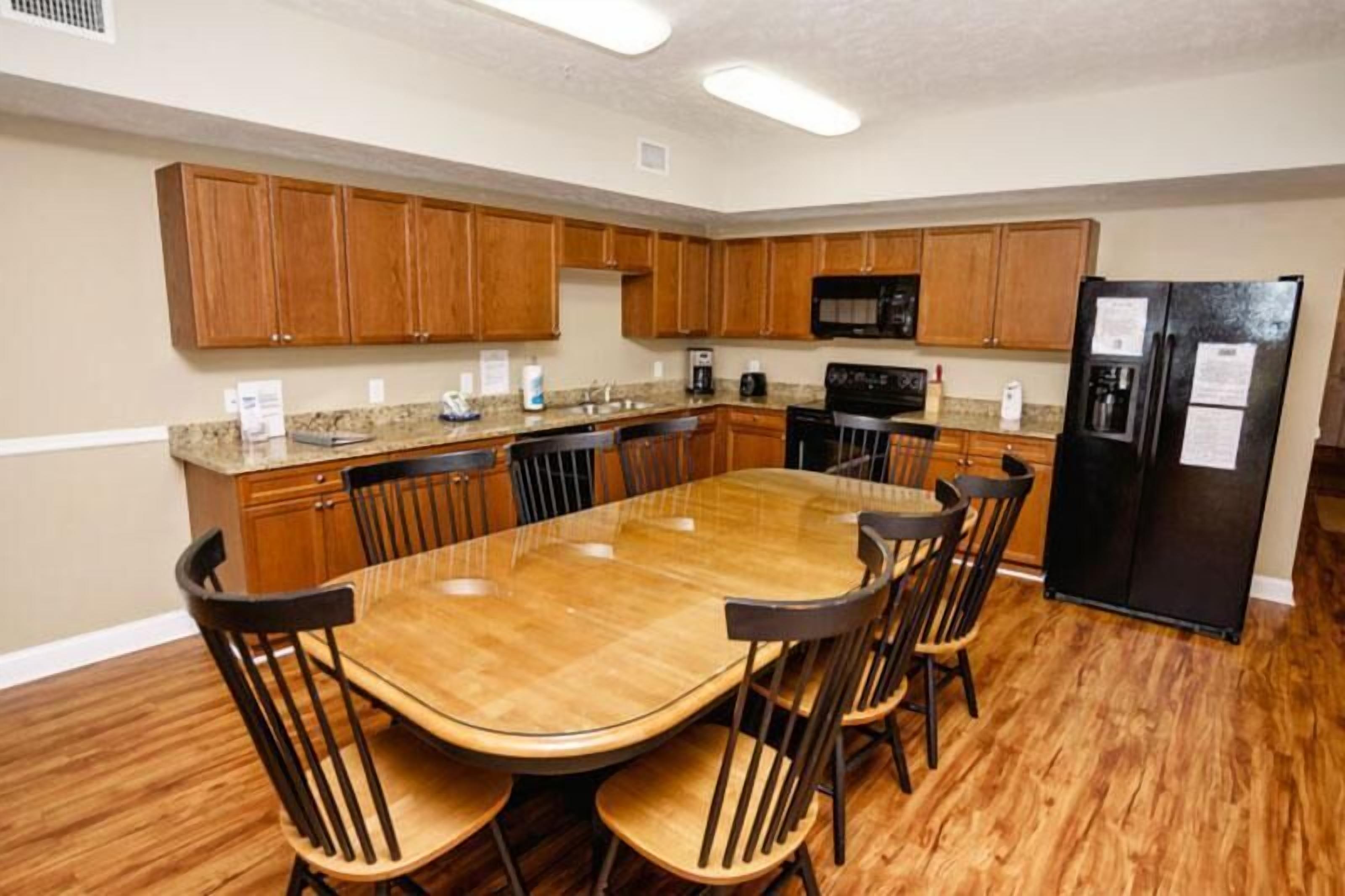 A kitchen with wooden cabinets, a black refrigerator, a microwave, and a dining table with chairs.
