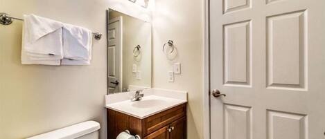A bathroom with a toilet, sink, and mirror. There is a towel rack with towels and a door with a handle.