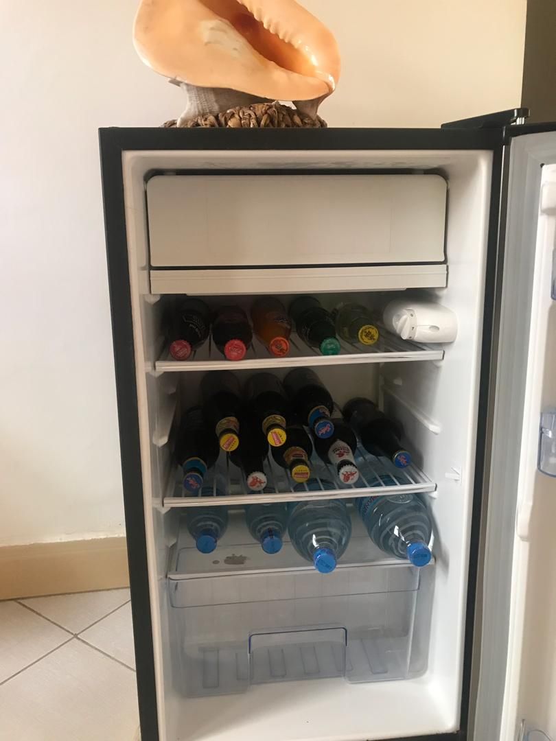 Een koelkast met meerdere planken, gevuld met flessen en een plastic bak.