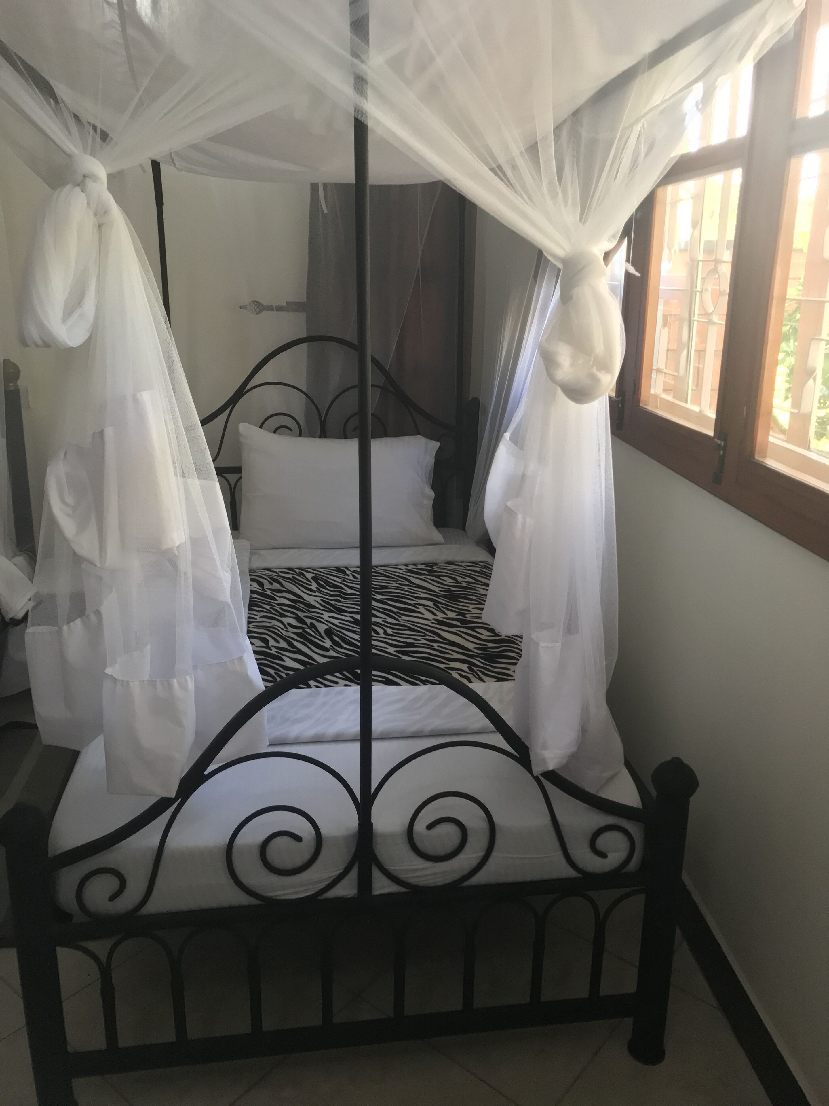 A bed with a black metal frame, white bedding, and a mosquito net.