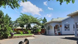 A house with a paved driveway, a covered porch, and a fenced yard with potted plants. - Le Parlour (Boma la Ngombe)