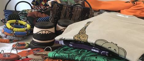 A variety of colorful textiles and accessories, including patterned fabrics, a giraffe-themed pillow, and beaded jewelry, displayed on a table.