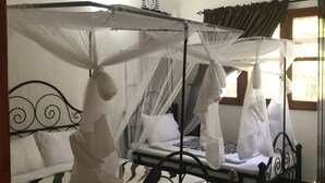 A room with two beds, each with a canopy. There is an air conditioning unit on the wall, a window with curtains, and a door with a keychain. - Le Parlour (Boma la Ngombe)