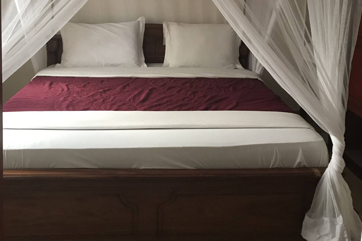 Ein Bett mit Baldachin, weiße Bettwäsche und eine marineblaue Tagesdecke.