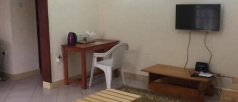 A room with a wooden bench, a small table, a white chair, a TV mounted on the wall, and a door leading to another room.