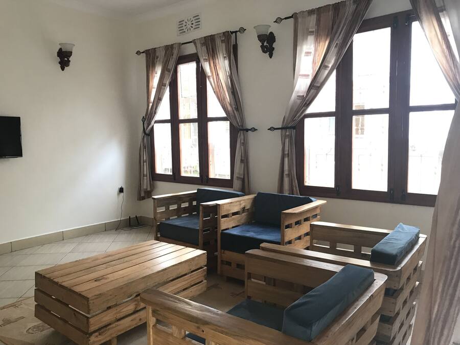 Una habitación con una zona de estar con banco de madera, una pequeña mesa y un televisor montado en la pared.