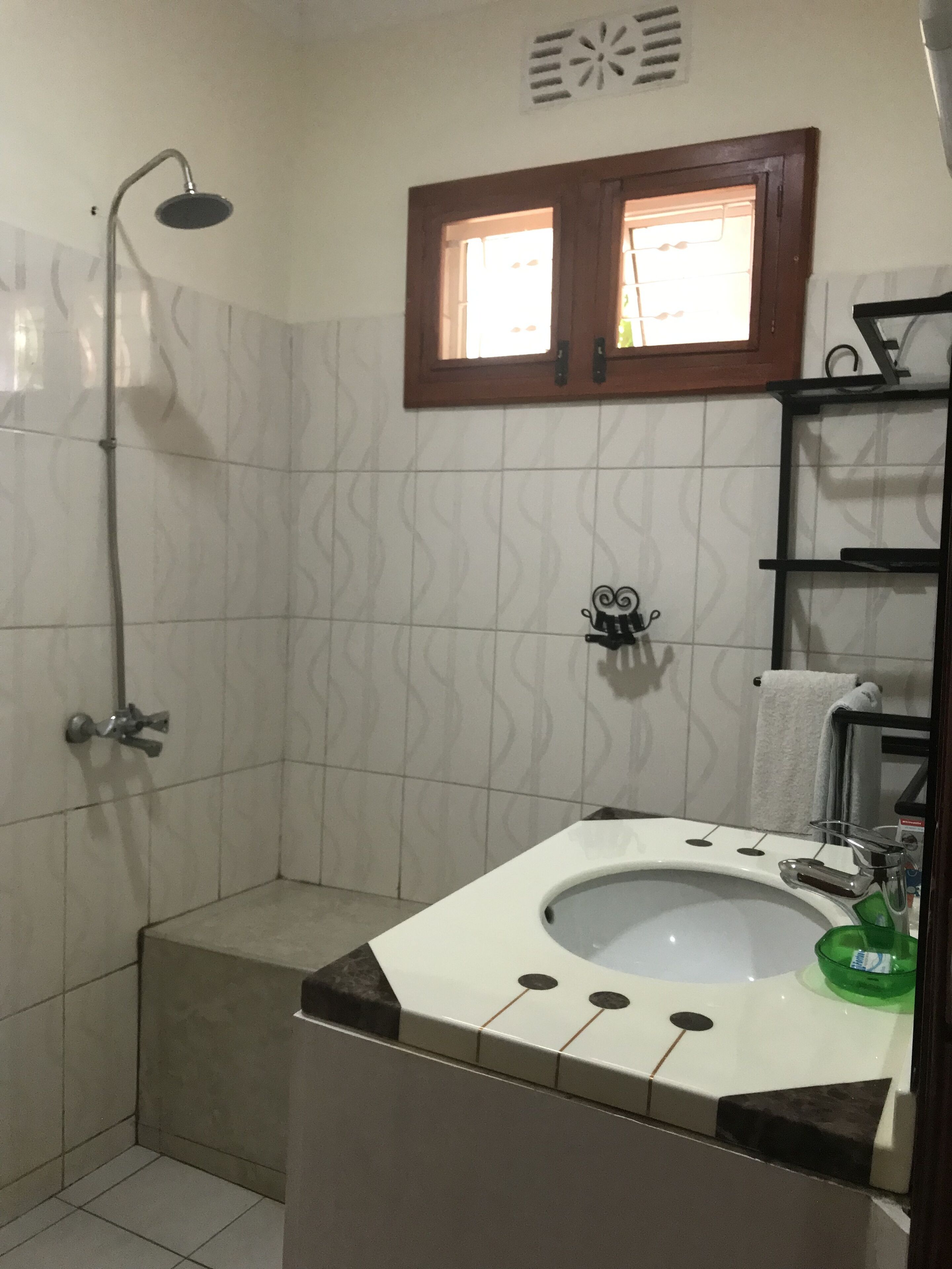 Ein Badezimmer mit Dusche, Waschbecken und einem grünen Seifenspender sowie einem Fenster über dem Waschbecken.