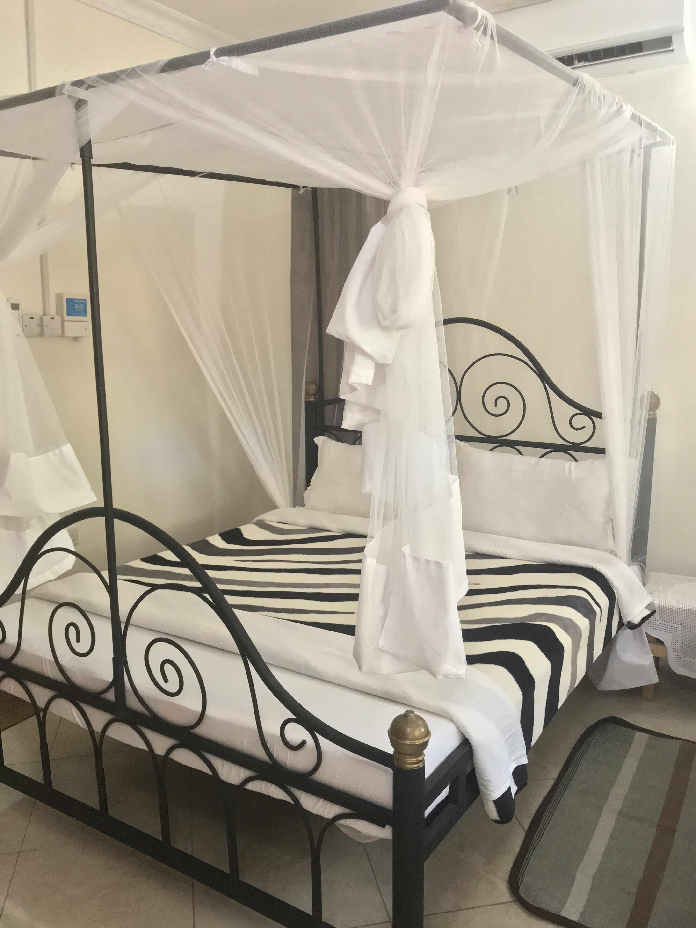 A four-poster bed with a canopy, a zebra-striped bedspread, and a bedside table with a lamp.